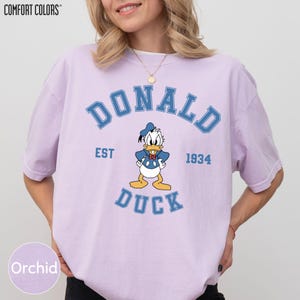 A woman wearing a pink t-shirt with a graphic of a cartoon duck and text that says "DONALD DUCK EST 1934".