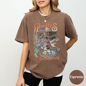 A woman wearing a brown t-shirt with a graphic of Disney characters and text related to the Pirates of the Caribbean ride at Disney World.