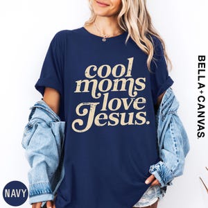 A woman wearing a navy blue t-shirt with the text "cool moms love Jesus" printed on it, along with a denim jacket.