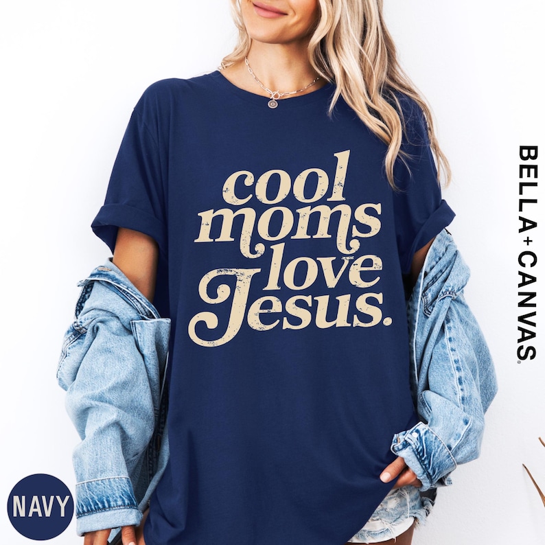 A woman wearing a navy blue t-shirt with the text "cool moms love Jesus" printed on it, along with a denim jacket.