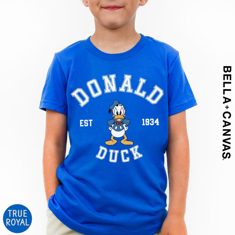 A young boy wearing a blue t-shirt with a cartoon image of Donald Duck and text that says "DONALD EST. 1934 DUCK".