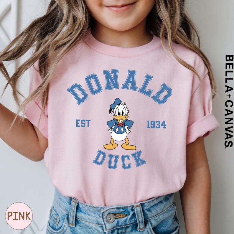A young girl wearing a pink t-shirt with a graphic of a cartoon duck and the text "DONALD DUCK EST 1934" printed on it.