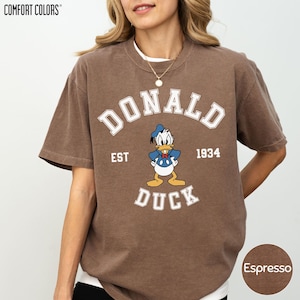 A woman wearing a brown t-shirt with a cartoon image of Donald Duck and text that says "DONALD DUCK EST. 1934".
