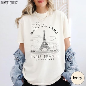 A woman wearing a white t-shirt with a graphic design of the Eiffel Tower and text that says "Magical Land Paris, France Disneyland".