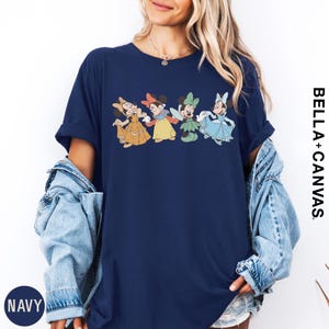 A woman wearing a navy blue t-shirt with a graphic of Disney Minnie Mouse characters, paired with a denim jacket and a necklace.