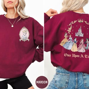 A woman wearing a burgundy sweatshirt with a Disney princess design on the front and back.