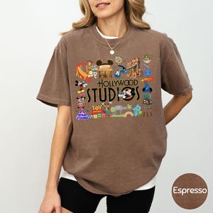 A woman wearing a brown t-shirt with various Disney and Pixar-themed graphics and text, including characters, logos, and phrases related to the Disney and Pixar brand.