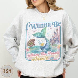 A woman wearing a gray sweatshirt with a colorful graphic design featuring a mermaid, castle, and text.