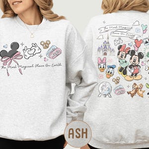 A woman wearing a white sweatshirt with various Disney characters and Disney-themed graphics printed on it.