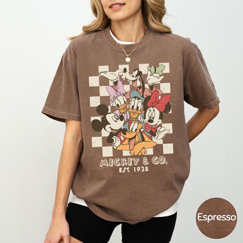 A woman wearing a brown t-shirt with a graphic of Disney characters and text.
