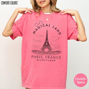A woman wearing a pink t-shirt with a graphic of the Eiffel Tower and text that says "Magical Land Paris, France Disneyland".