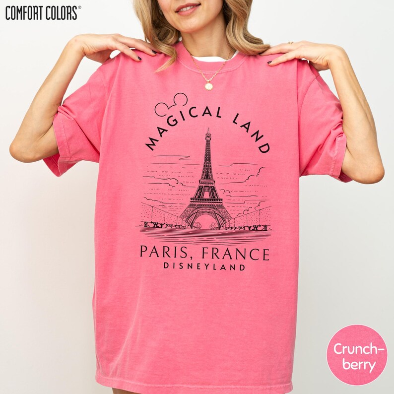 A woman wearing a pink t-shirt with a graphic of the Eiffel Tower and text that says "Magical Land Paris, France Disneyland".