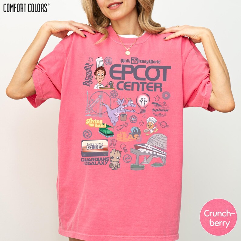 A woman wearing a pink t-shirt with various Disney-themed graphics and text, including a chef, a rocket ship, and other iconic elements associated with the Epcot Center.
