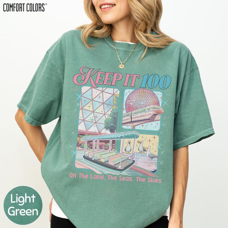 A woman wearing a green t-shirt with a graphic design featuring a large dome, a boat, and a beach scene.