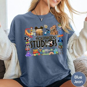 A woman wearing a blue t-shirt with various Disney and Hollywood-themed graphics and text, including characters, landmarks, and promotional logos.