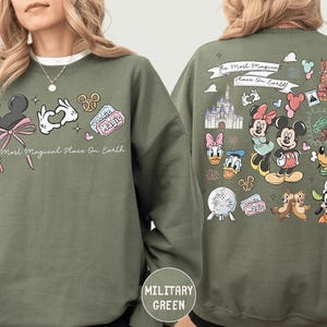 A woman wearing a green sweatshirt with various Disney characters and Disney-themed graphics printed on it.