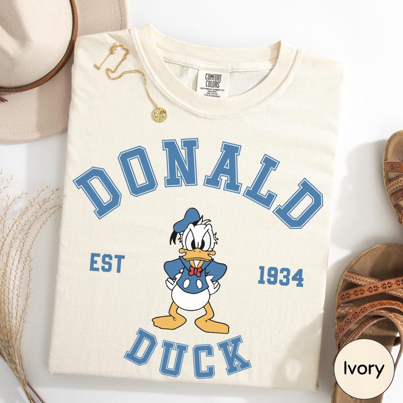 a white t-shirt with a graphic of a cartoon duck and the text "DONALD DUCK EST 1934".