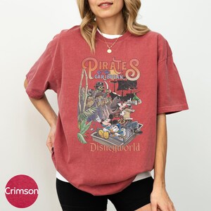 A woman wearing a red t-shirt with a graphic of Disney characters from the Pirates of the Caribbean franchise.