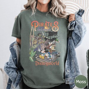 A person wearing a green t-shirt with a graphic design of Disney characters from the Pirates of the Caribbean ride at Disneyworld.