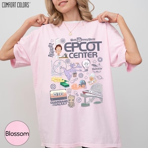 A woman wearing a pink t-shirt with various Disney-themed graphics and text, including characters, logos, and other iconic elements associated with the Walt Disney World Epcot Center.