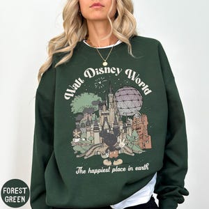 A woman wearing a green sweatshirt with a graphic of Disney World and the text "The happiest place in earth" printed on it.