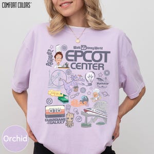 A woman wearing a purple t-shirt with various Disney-themed graphics and logos, including a chef, a roller coaster, and other iconic Disney characters and landmarks.