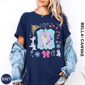 A woman wearing a navy blue t-shirt with a graphic of Olaf from the Disney movie Frozen. She is also wearing a denim jacket and has her hands in her pockets.