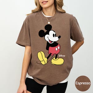A woman wearing a brown t-shirt with a Mickey Mouse graphic printed on it.