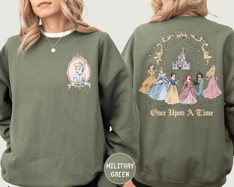 A woman wearing a green sweatshirt with a graphic of a group of princesses and a castle on the back.