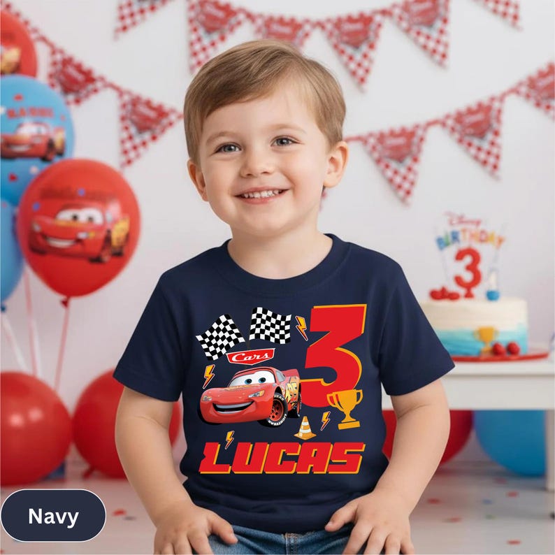 A young boy wearing a navy blue t-shirt with a Cars-themed design, smiling at the camera.