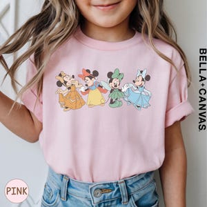 A young girl wearing a pink t-shirt with a graphic of four Disney Minnie Mouse characters.