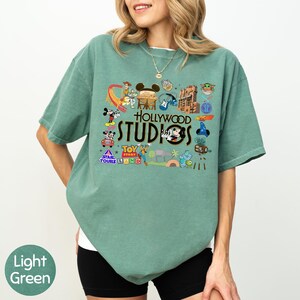 A woman wearing a green t-shirt with various Disney and Hollywood-themed graphics and text printed on it.