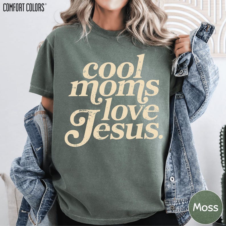 A woman wearing a green t-shirt with the text "cool moms love Jesus" printed on it, along with a denim jacket.
