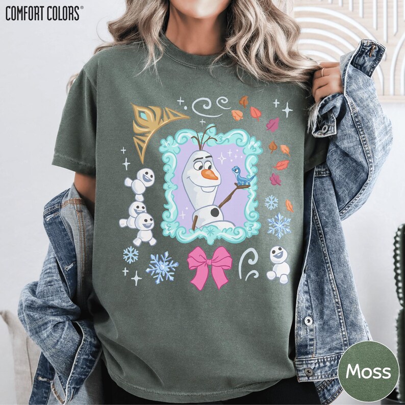 A person wearing a green t-shirt with a graphic design featuring a character from the Disney movie Frozen, surrounded by various elements such as snowflakes, stars, and a bow.