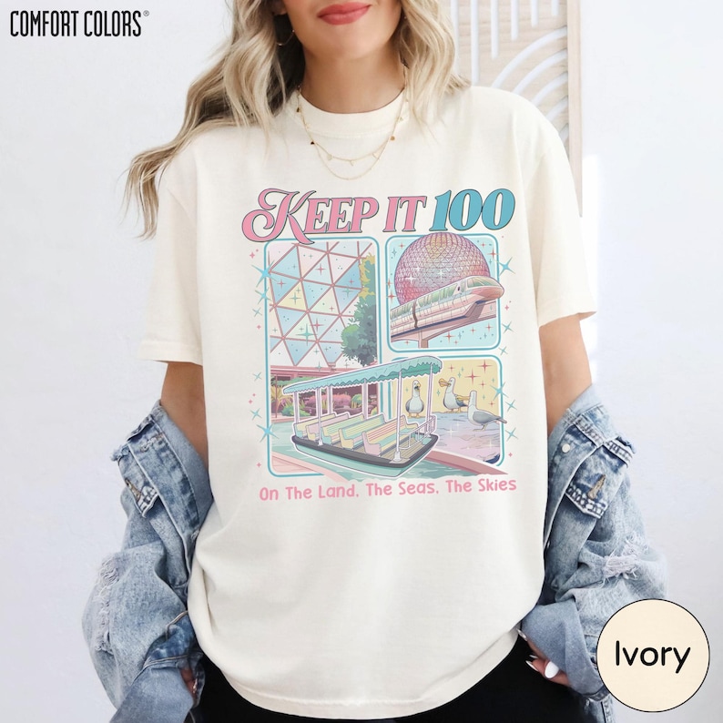 A woman wearing a white t-shirt with a colorful graphic design featuring a dome, a boat, and a beach scene.