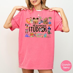 A woman wearing a pink t-shirt with various Disney and Hollywood-themed graphics and text.