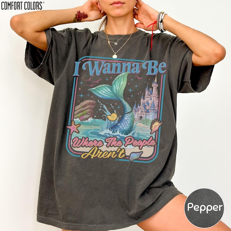 A person wearing a black t-shirt with a graphic design featuring a mermaid and a castle.