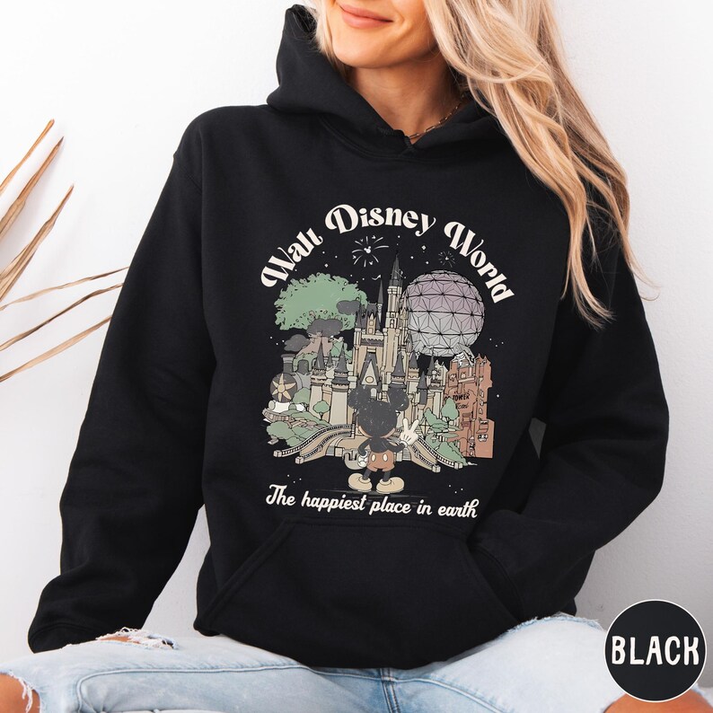 A woman wearing a black hoodie with a graphic design of various Disney landmarks and the text "The happiest place in earth" printed on it.