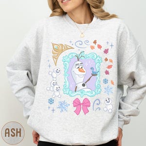 A woman wearing a gray sweatshirt with a colorful graphic design featuring characters from the Disney movie Frozen.