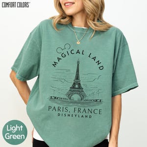 A woman wearing a green t-shirt with a graphic of the Eiffel Tower and the text "Magical Land Paris, France Disneyland" printed on it.