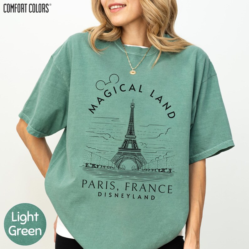 A woman wearing a green t-shirt with a graphic of the Eiffel Tower and the text "Magical Land Paris, France Disneyland" printed on it.