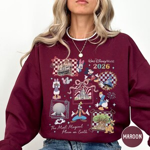 A woman wearing a burgundy sweatshirt with a Disney World-themed design, including various Disney characters and landmarks.