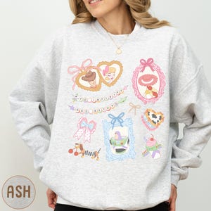 A woman wearing a gray sweatshirt with various cartoon-style illustrations and text on it.