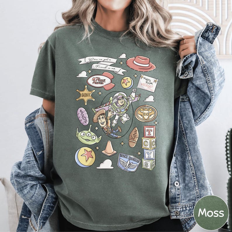 A person wearing a green t-shirt with various cartoon characters and icons, including a character from the Toy Story franchise, a character from the Star Wars franchise, and a character from the Toy Story series.