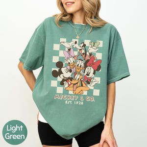 A woman wearing a green t-shirt with a graphic of Disney characters and text.