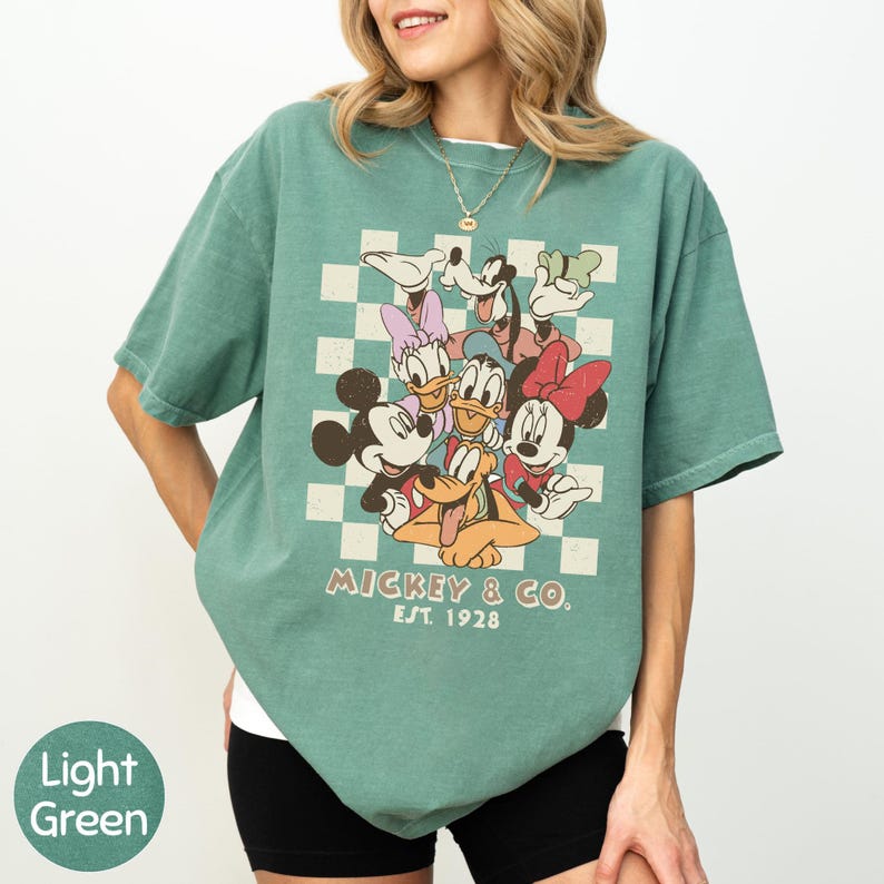 A woman wearing a green t-shirt with a graphic of Disney characters and text.