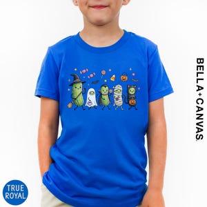 A young boy wearing a blue t-shirt with a Halloween-themed graphic of various cartoon characters, including a witch, ghost, mummy, and pumpkin.