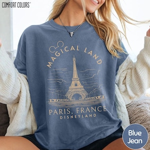 A woman wearing a blue t-shirt with a graphic design of the Eiffel Tower and text that says "Magical Land Paris, France Disneyland".