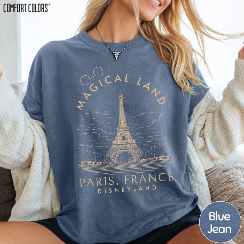 A woman wearing a blue t-shirt with a graphic design of the Eiffel Tower and text that says "Magical Land Paris, France Disneyland".