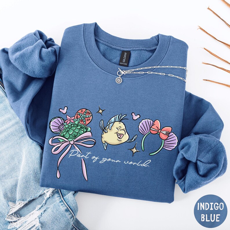 A blue sweatshirt with a cartoon character and text printed on it, along with a necklace and some other clothing items.